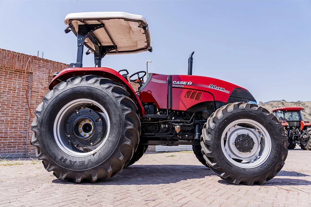 Tractor agrícola Case IH 90JXM rojo con toldo blanco, vista lateral en patio de maquinaria.