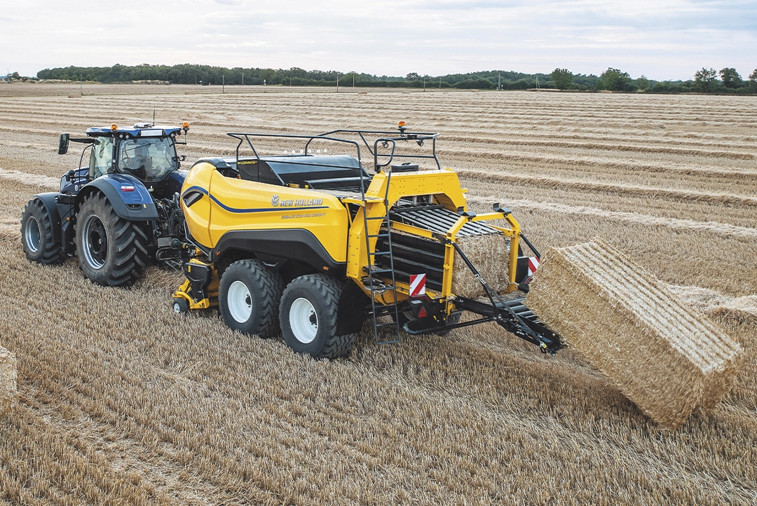 Tractor azul remolcando la empacadora gigante BigBaler 1290 High Density al momento de expulsar una