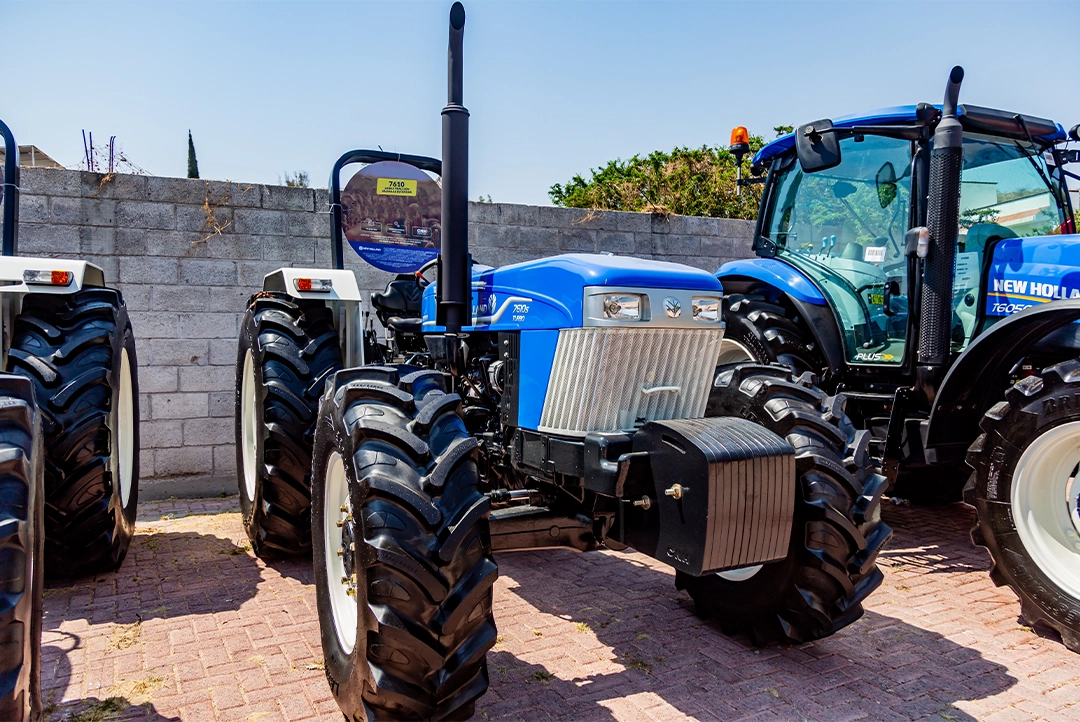 Vista tres cuartos frontal del tractor New Holland 7610S Herencia exhibido en patio con contrapesos