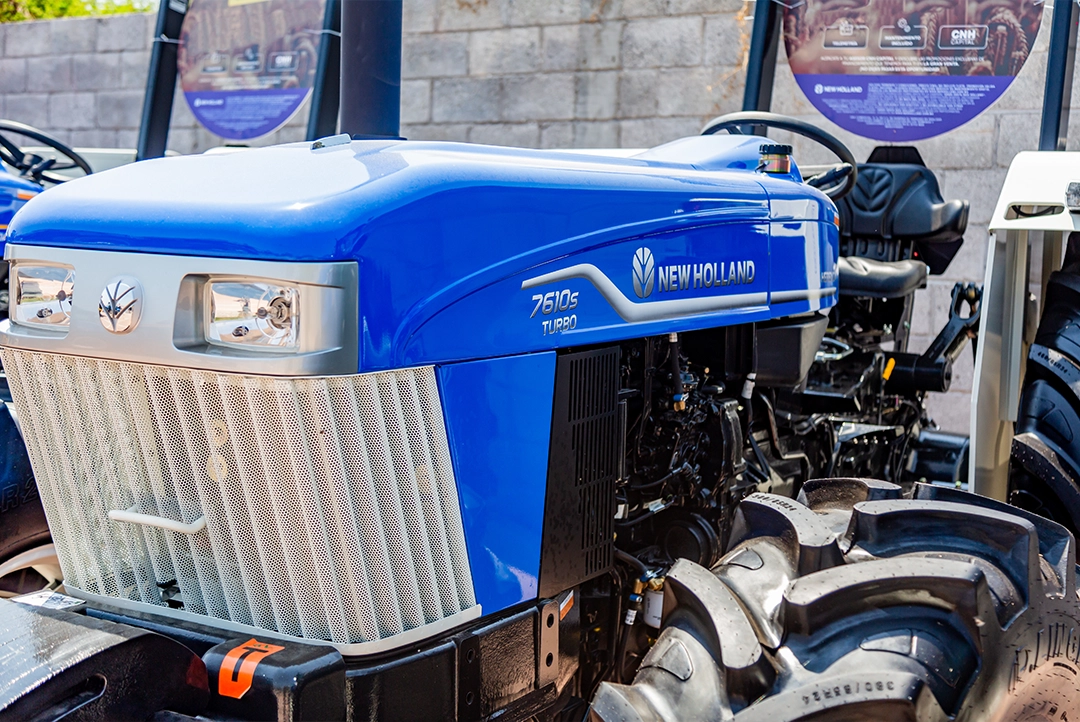 Detalle del cofre azul, parrilla frontal y neumático delantero del tractor New Holland 7610S Herenci