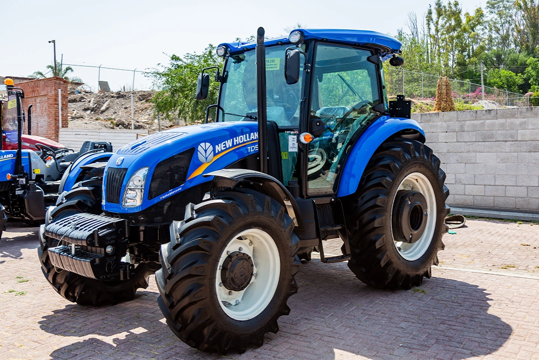 Tractor agrícola New Holland TD5.110 azul con cabina estacionado en patio de exhibición.