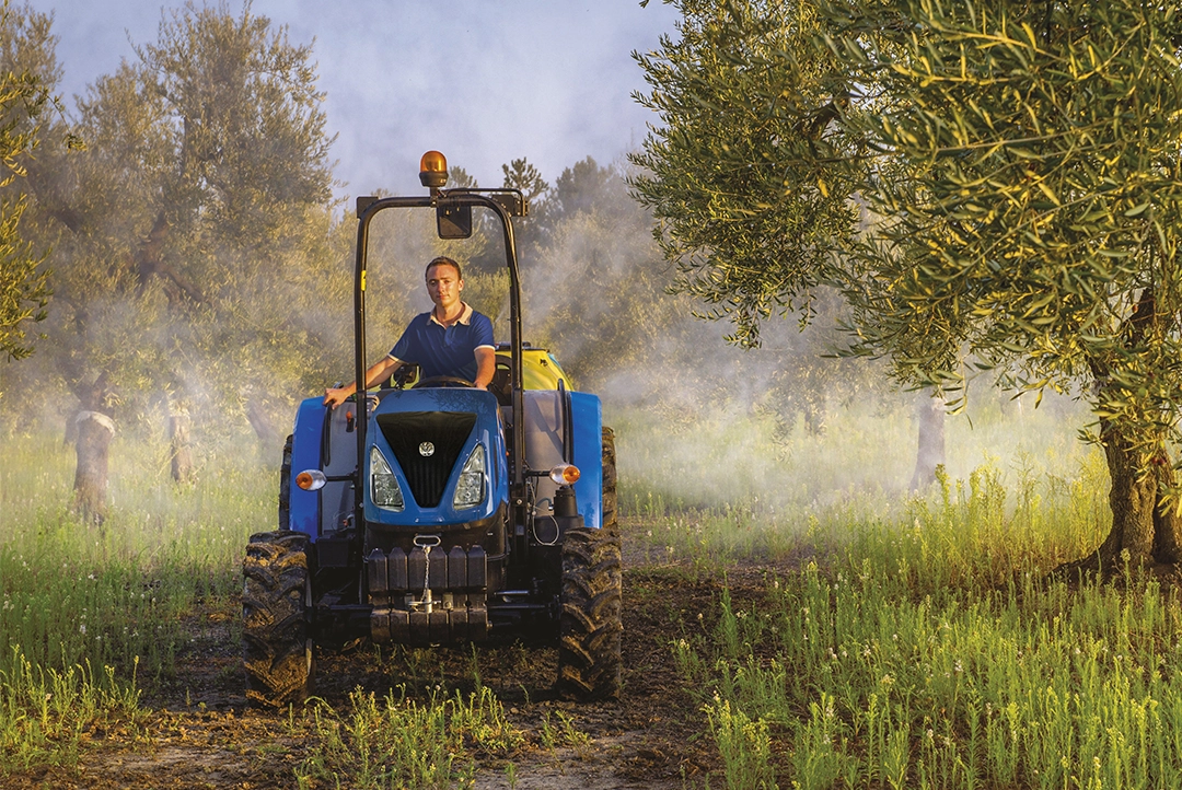 Tractor New Holland TD85F realizando labores de fumigación en un huerto de árboles.