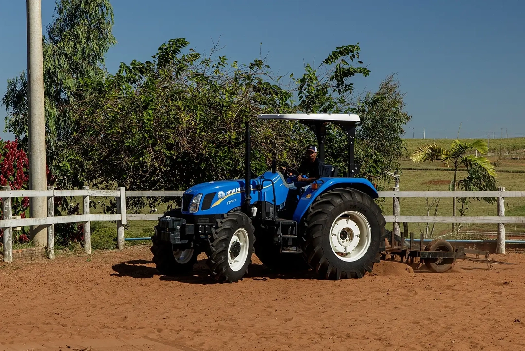 Tractor agrícola New Holland TT4.75 azul con toldo trabajando el suelo en un picadero