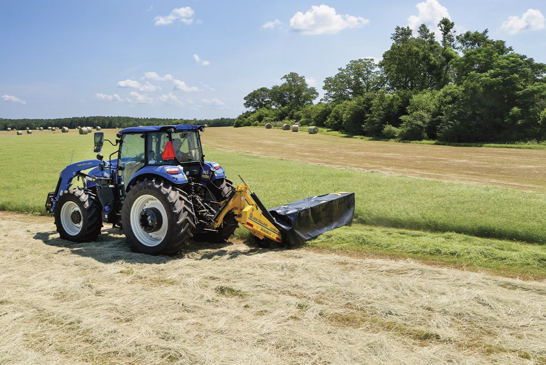Tractor azul operando una segadora de discos DuraDisc 108M en un campo de forraje.